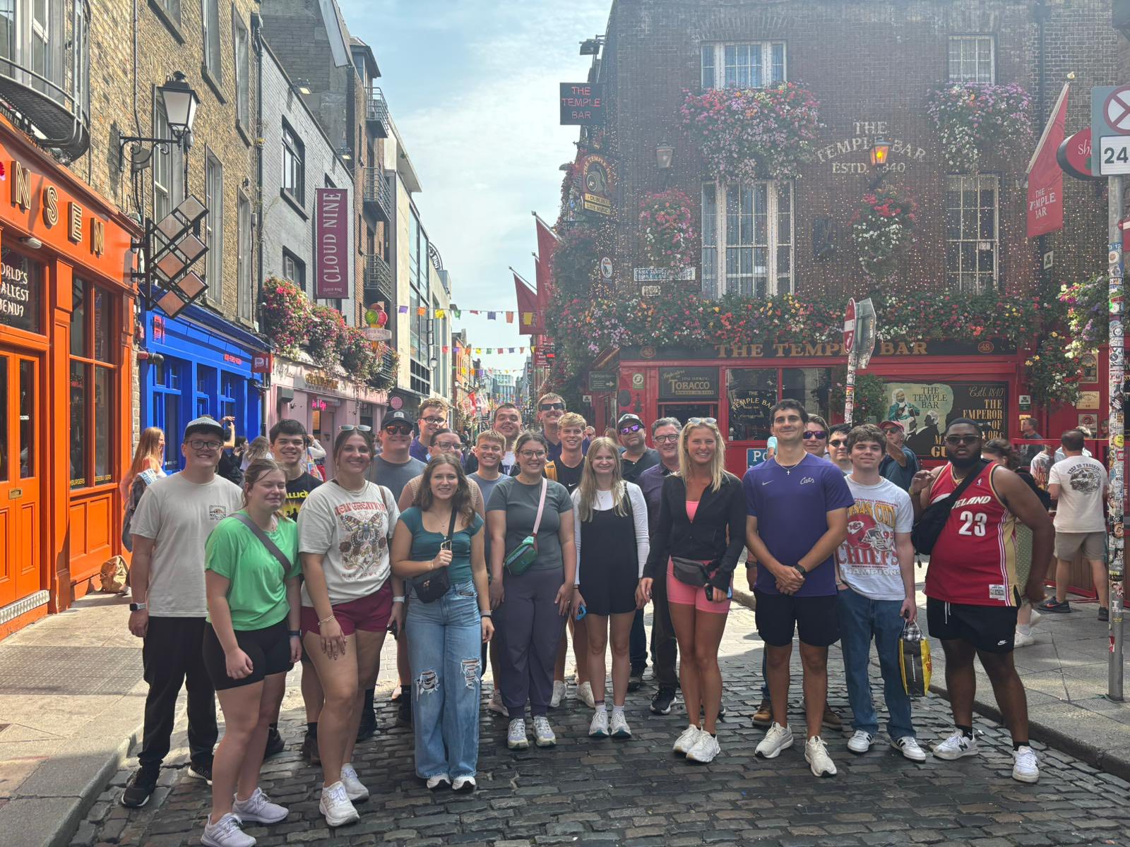 A group of students pose for a portrait in a line along a colorful Irish street.