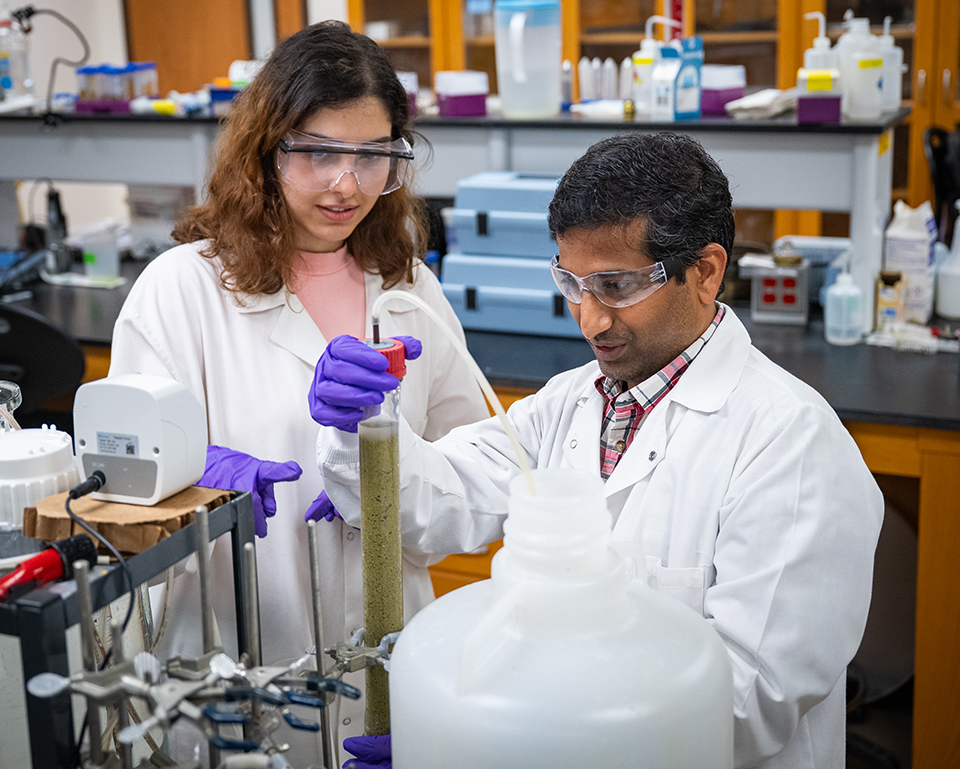 A student and a college professor researcher work in a lab, examining a vial.