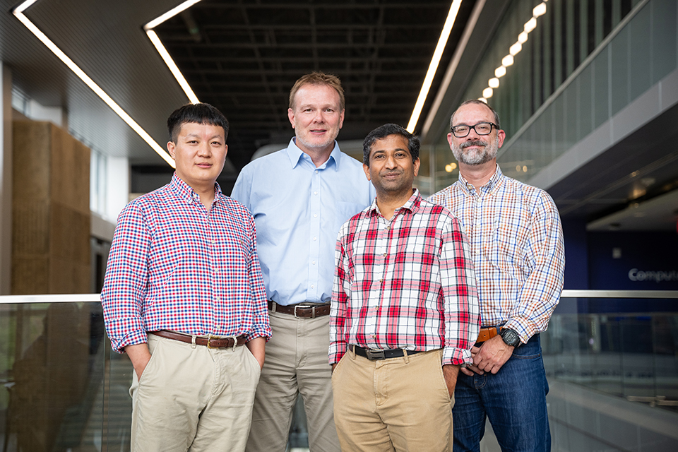A group of four researchers dressed in plaid button-up shirts pose for a group portrait.