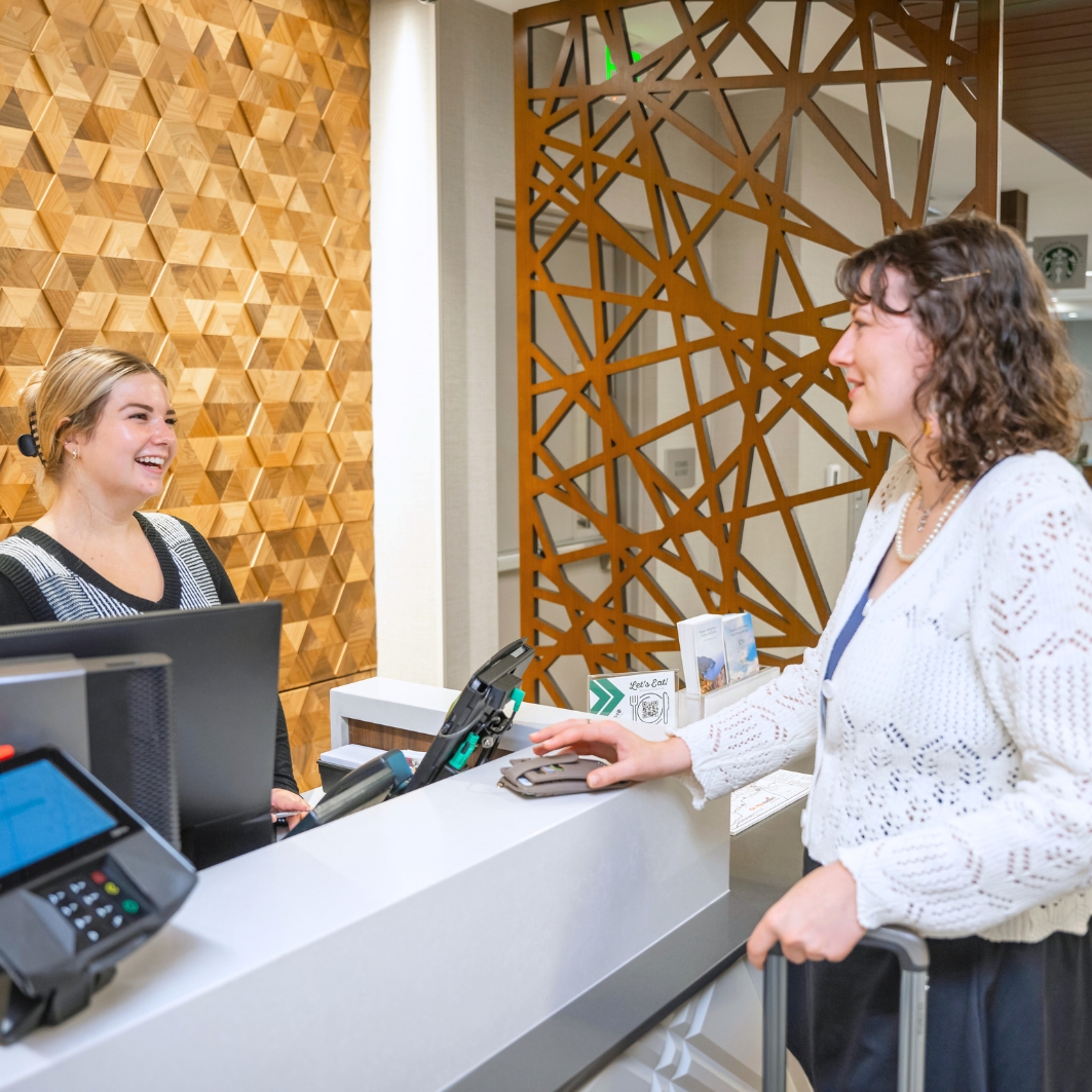 Two women speak from opposite sides of a hotel welcome desk