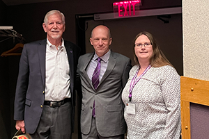 Two men stand with a woman and pose for a photo after a symposium.