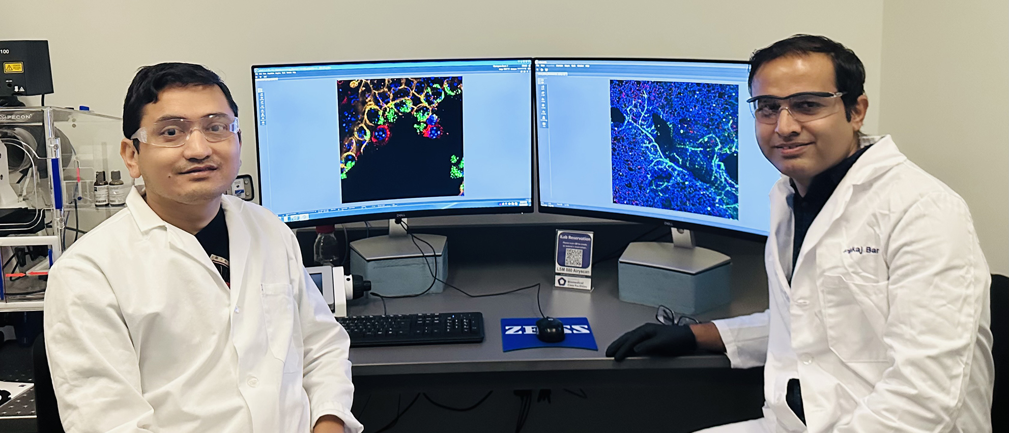 Two university researchers sit at a computer station and pose for a portrait.