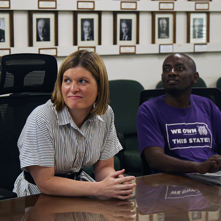 A woman professor sits and watches an off-screen presentation next to a student.
