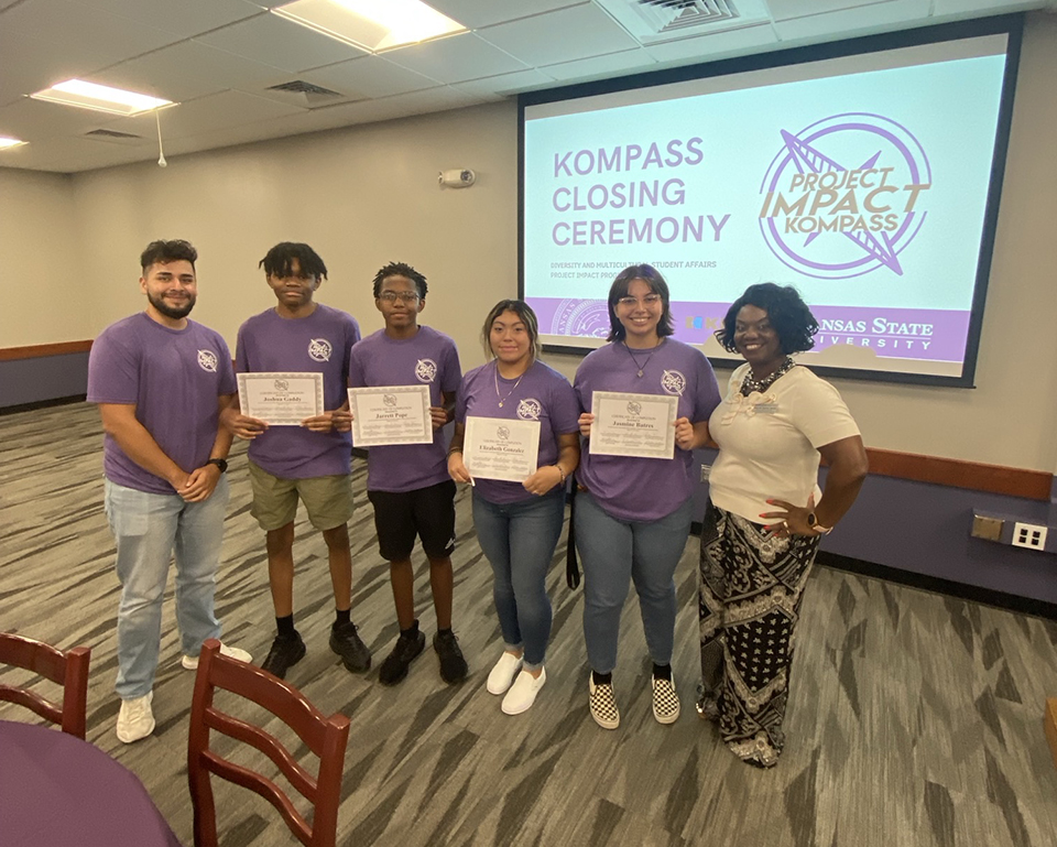A college advisor poses with a small group of college students in a conference room.