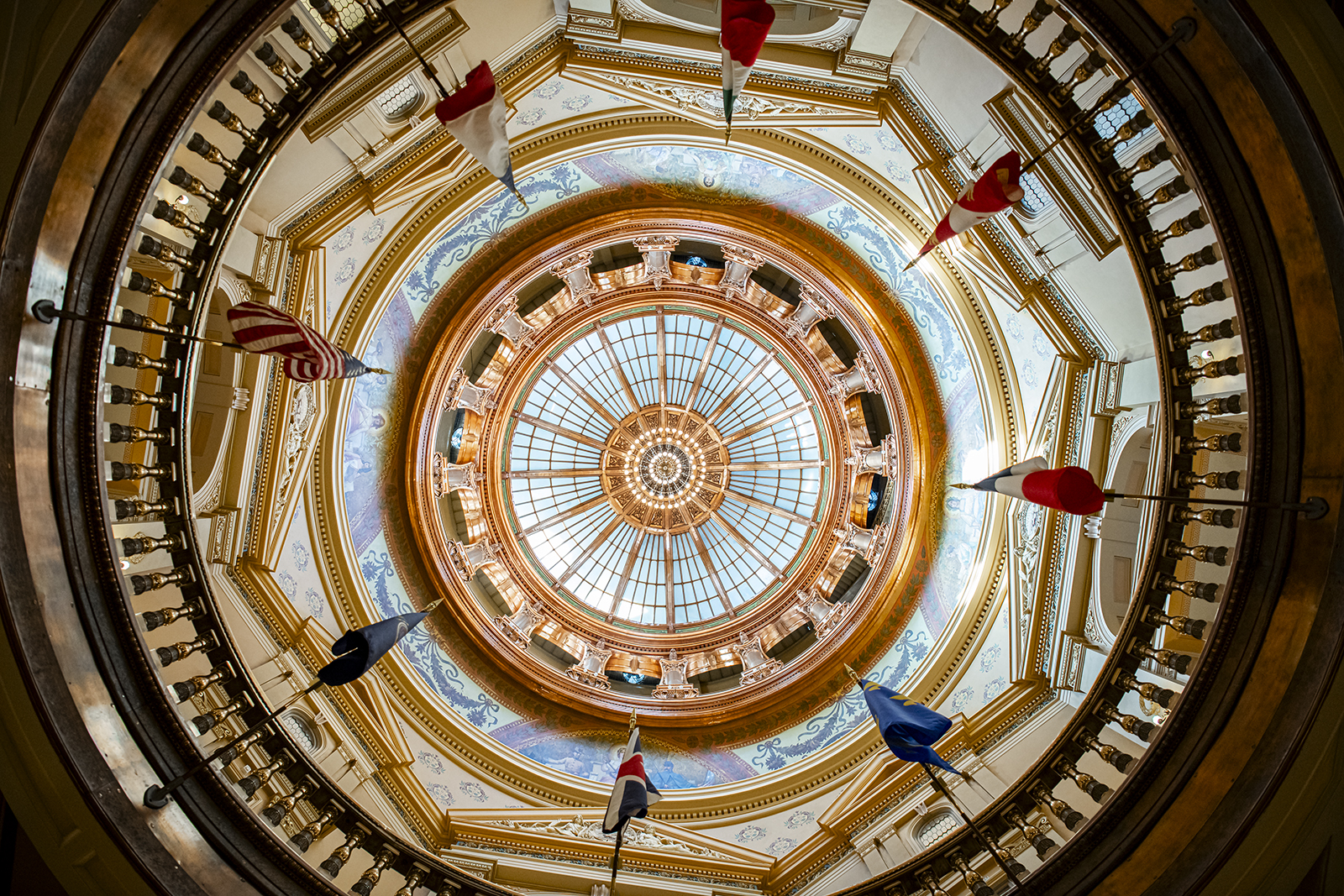 An underneath view shows the circular and brightly lit roof of the Kansas Capitol rotunda.