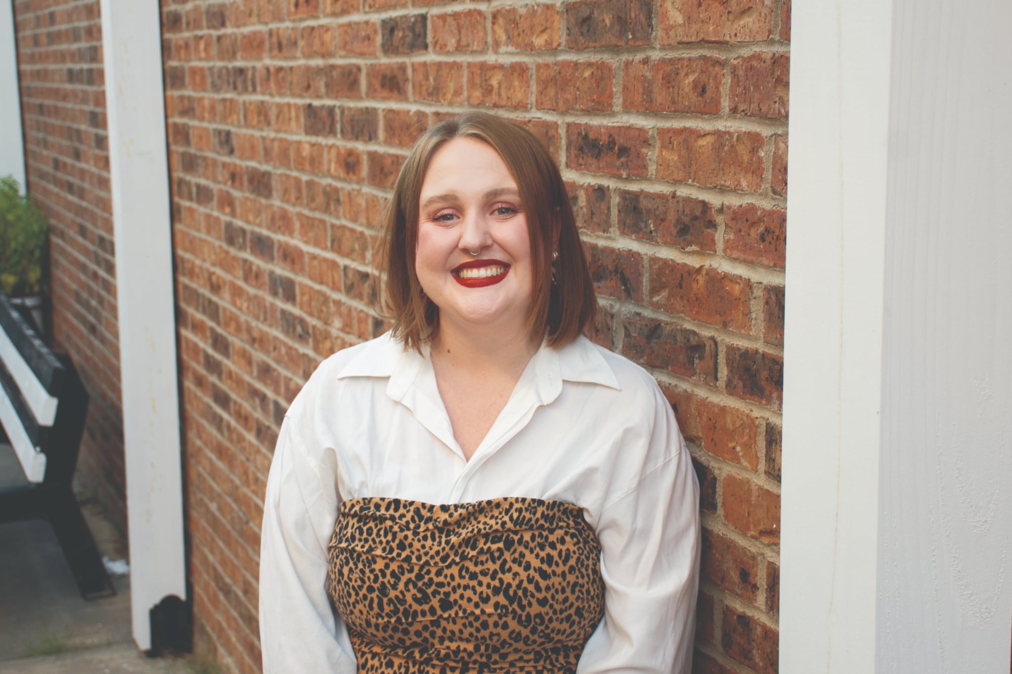 Kimberlee Westcott smiles for a portrait in front of a building with a red brick wall.