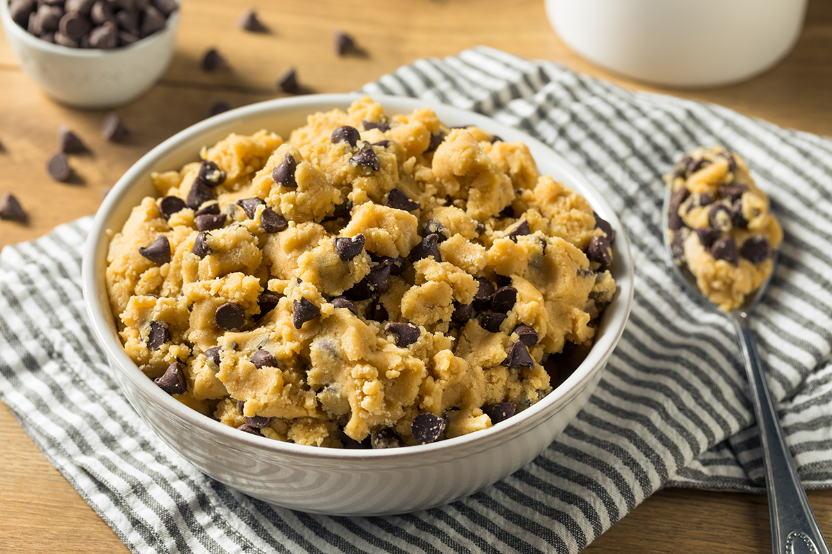 A spoonful of cookie dough sits on top of a towel and next to a bowl full of cookie dough.