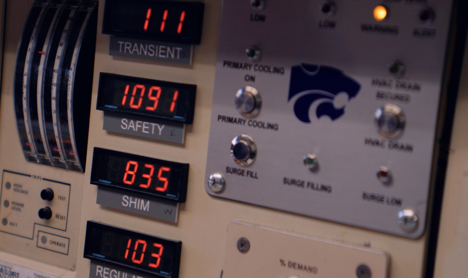 A closeup of a K-State nuclear control panel, with lights, switches and a purple powercat.