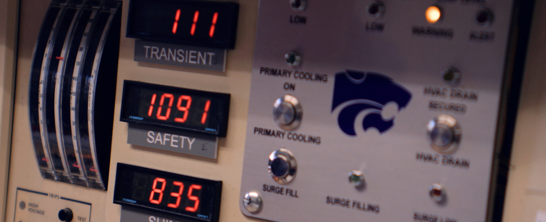 A closeup of a K-State nuclear control panel, with lights, switches and a purple powercat.