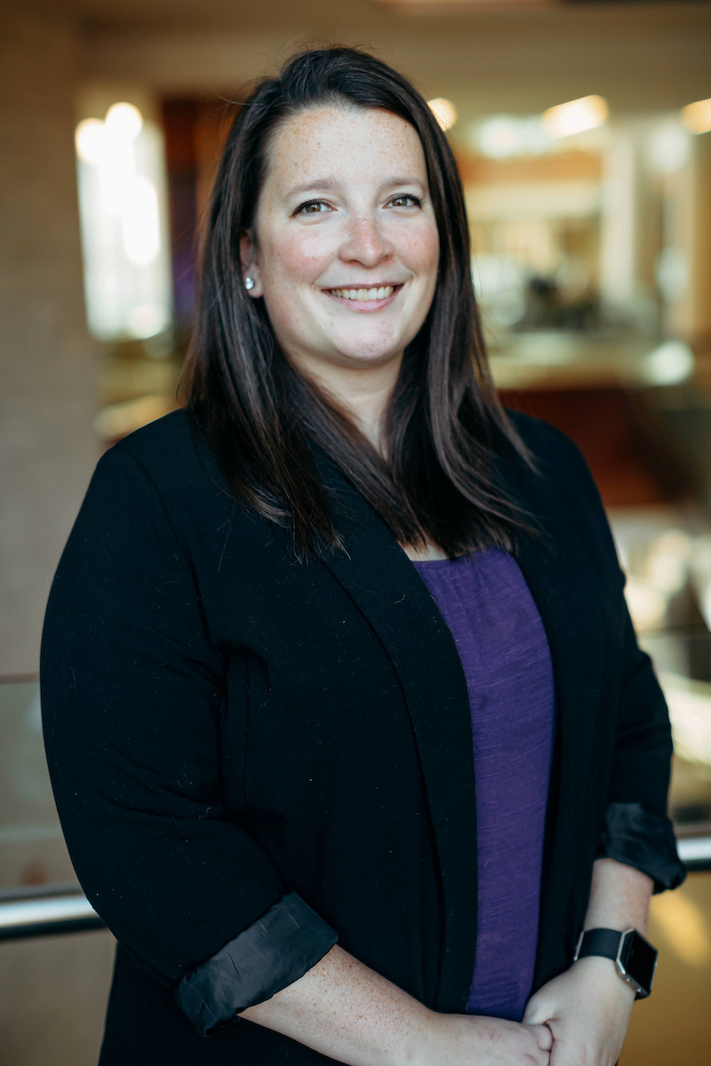 Megan Ronnebaum, wearing a purple shirt and black blazer, poses for a headshot in the K-State College of Business.