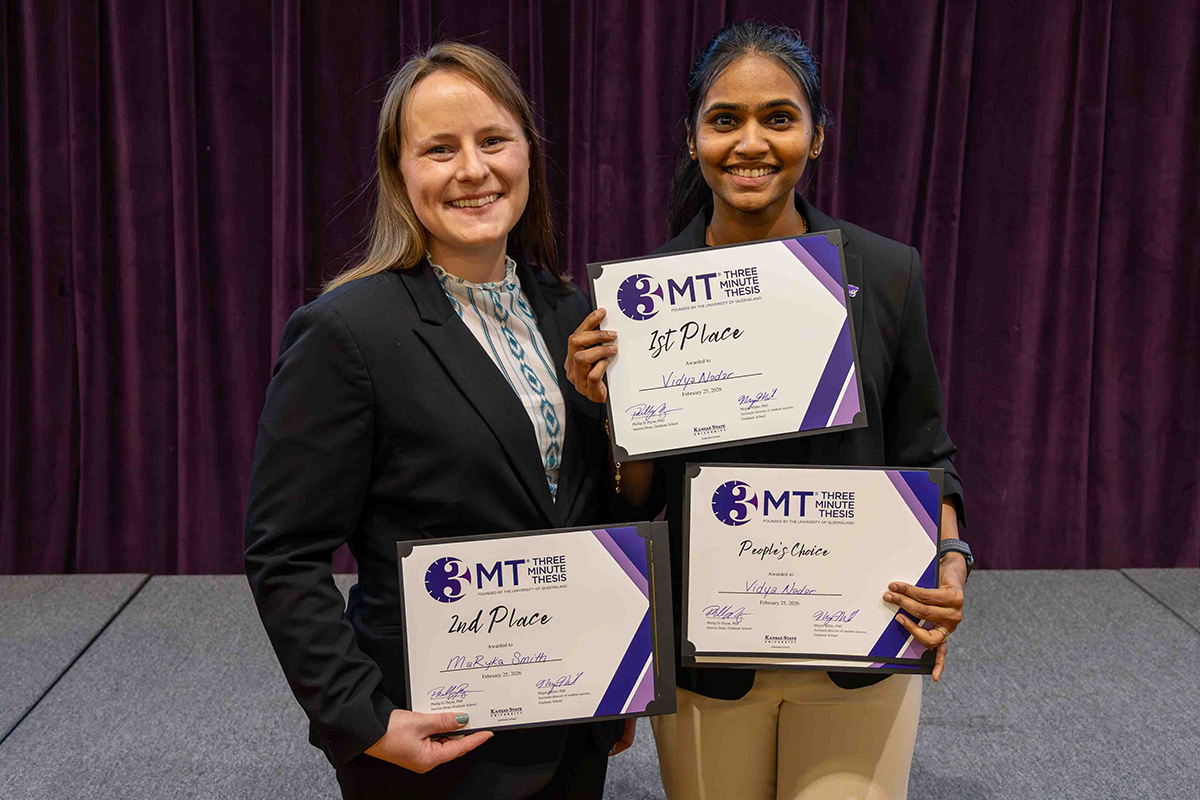 Two female doctoral students in business attire pose for a portrait and hold certificates that show them as first and second place winners, as well as a People's Choice recipient, for a research competition.