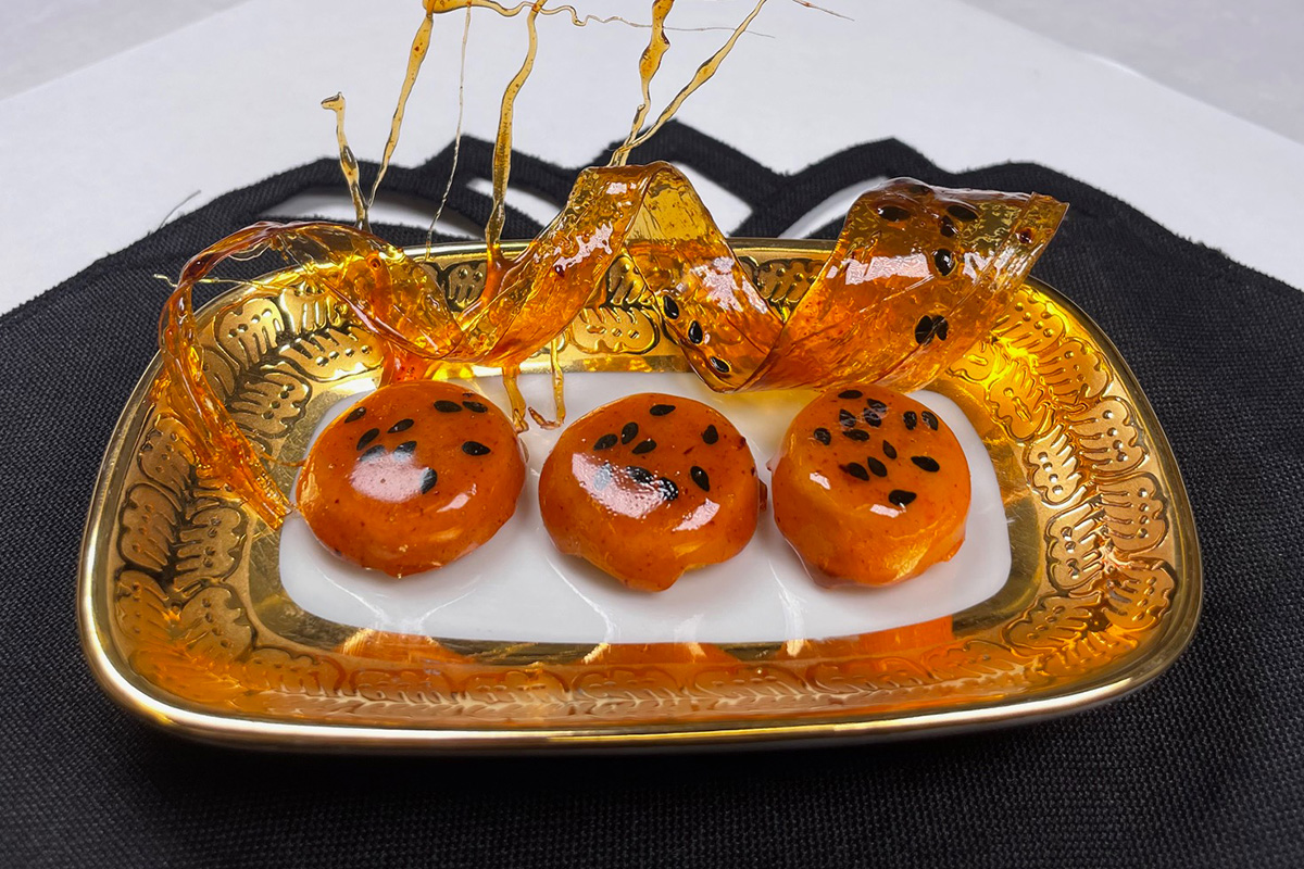 A close-up image of three shortbread cookies on display at a conference waiting to be judged. The cookies have an orange glaze over them with small dark seeds in the glaze.