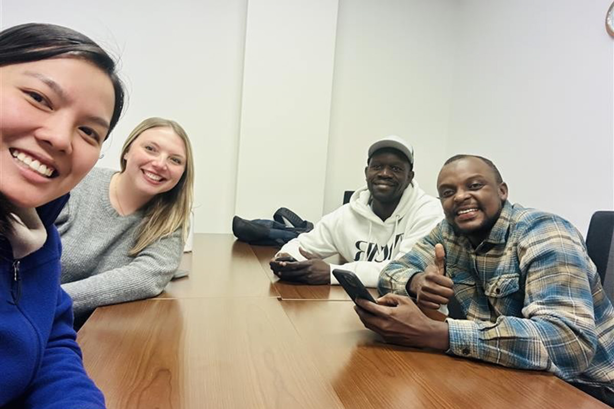 Four college students smile for a selfie while sitting around a conference table.