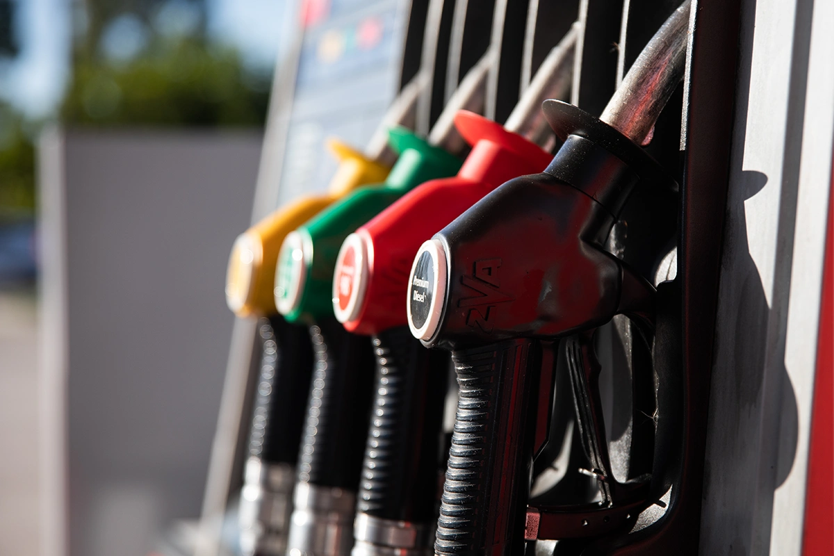 A close up shot shows a row of gas pump nozzles in heavy shadow from a setting sun.