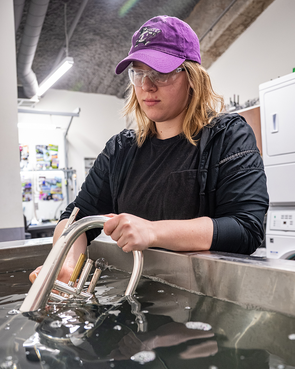 A female college student pulls a melophone out of a steel tub filled with clear, but grayish-blue, liquid.