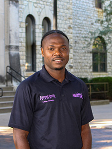 Jonathan Maka smiles for a portrait outside a limestone building.