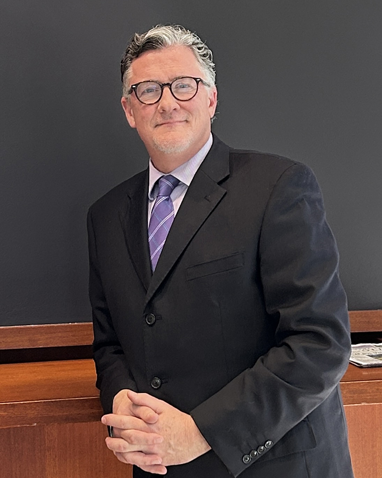  A male college professor in a suit poses for a portrait.
