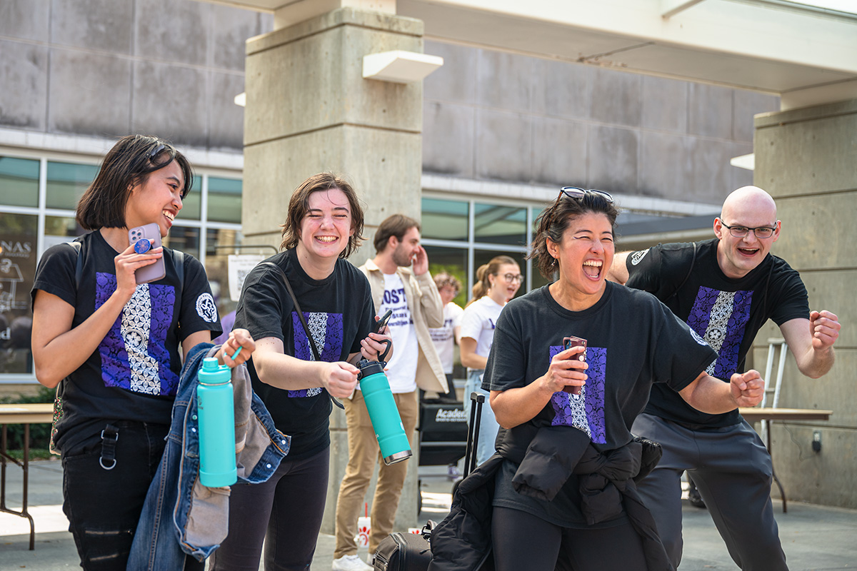 Four people in black shirts with purple and white designs do the Wabash dance at K-State Open House.