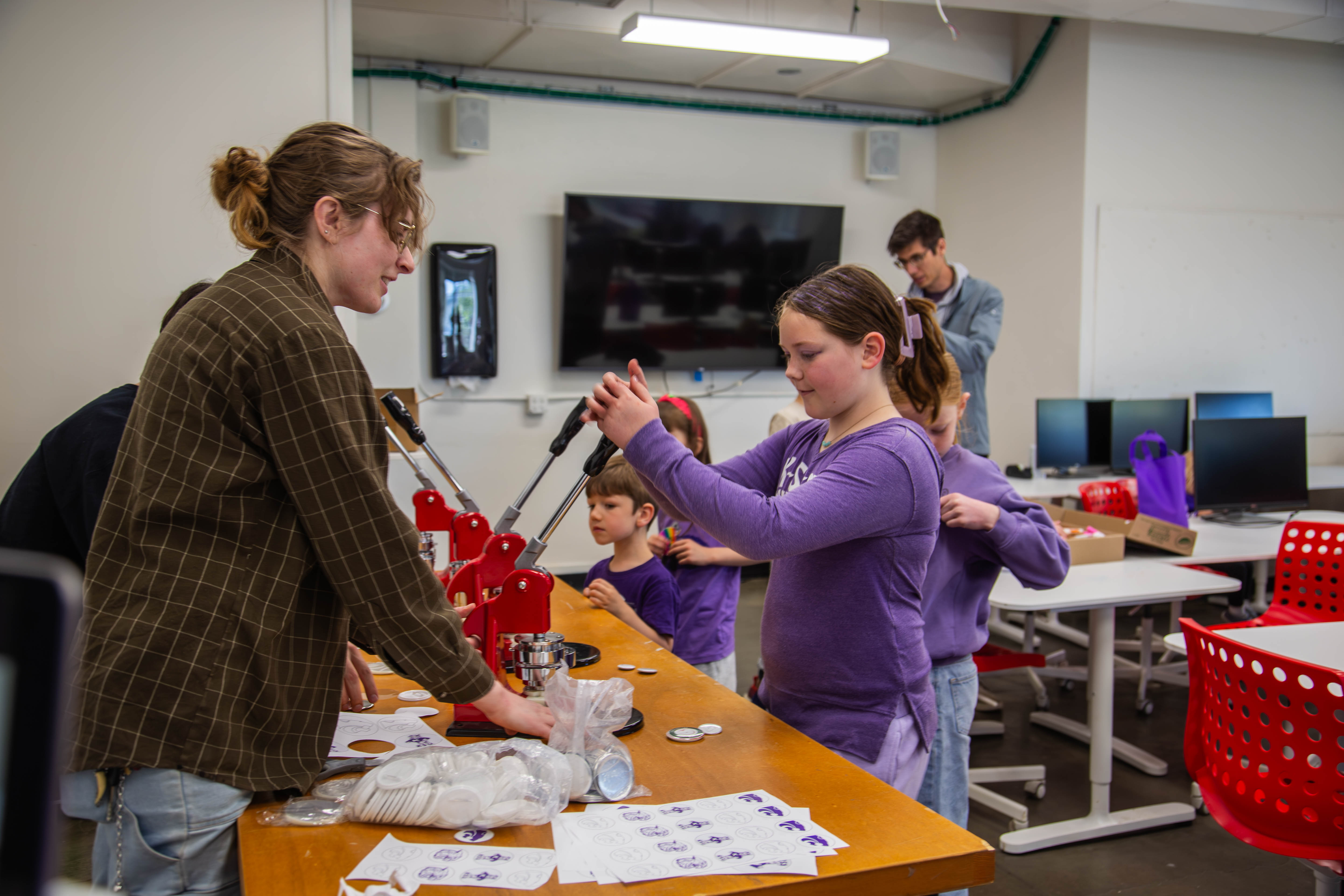 A Kansas State student helps children make buttons during a hands-on activity in a campus classroom. 