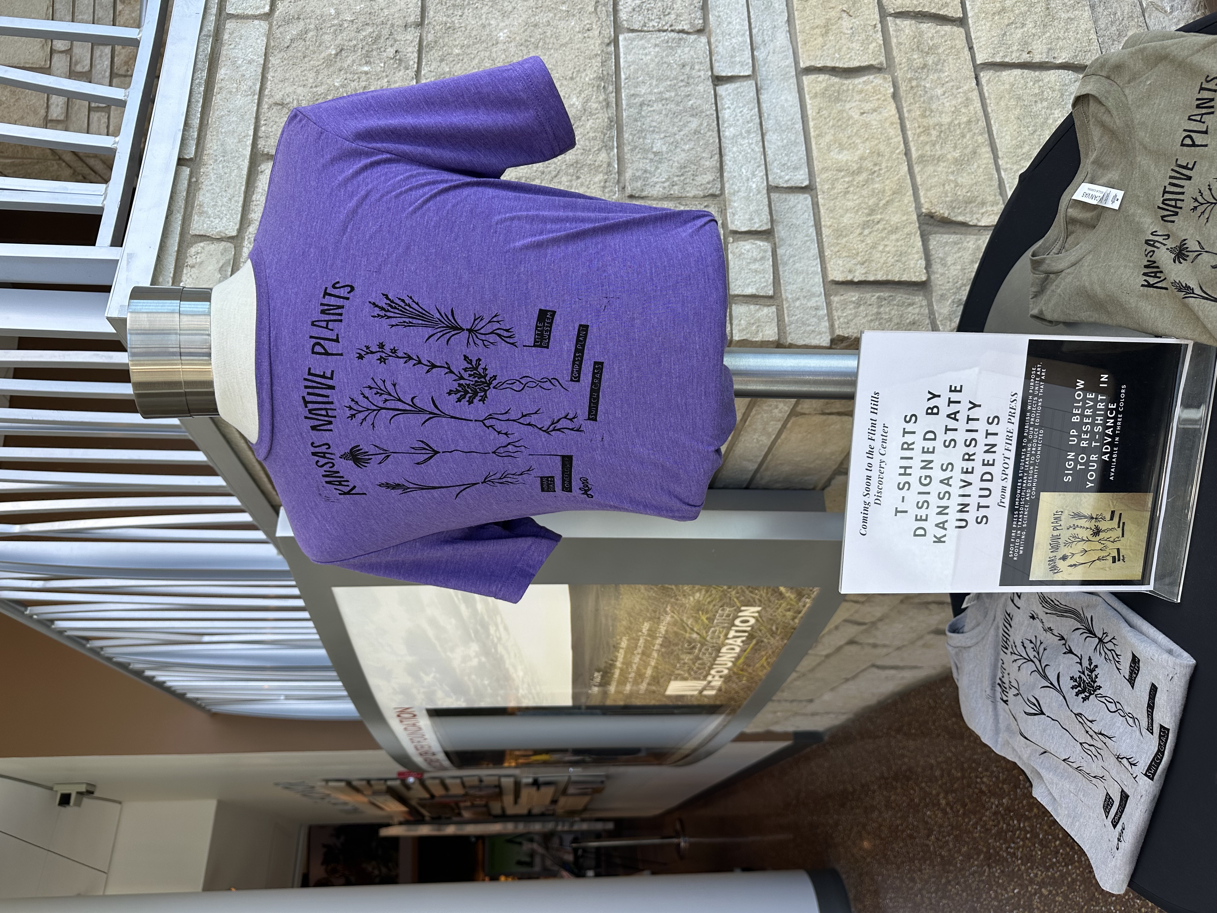 A purple shirt that says Kansas Native Plants on it is displayed with similar shirts in different colors. Cutline: