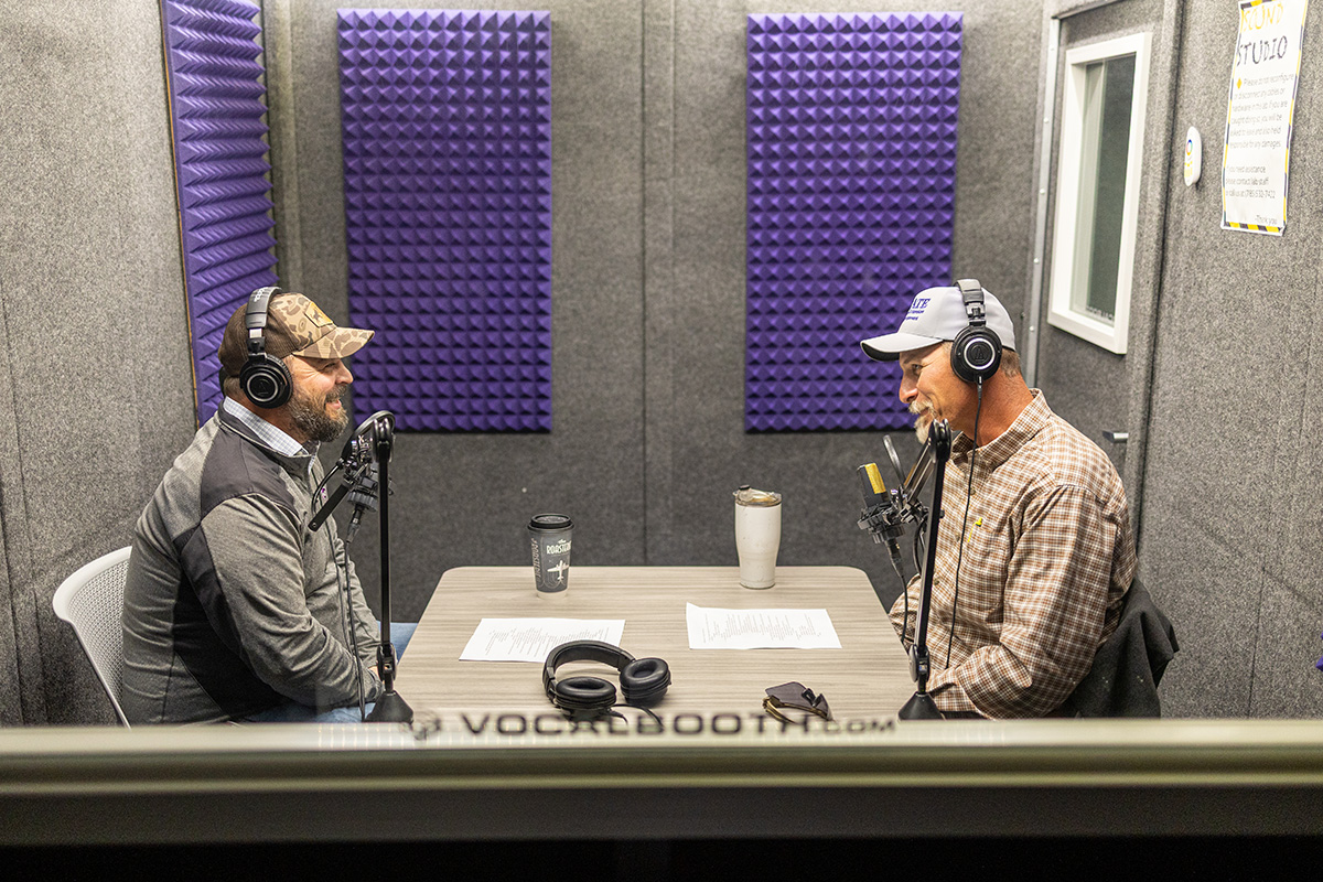 Two men sit facing each other in a podcast studio. 