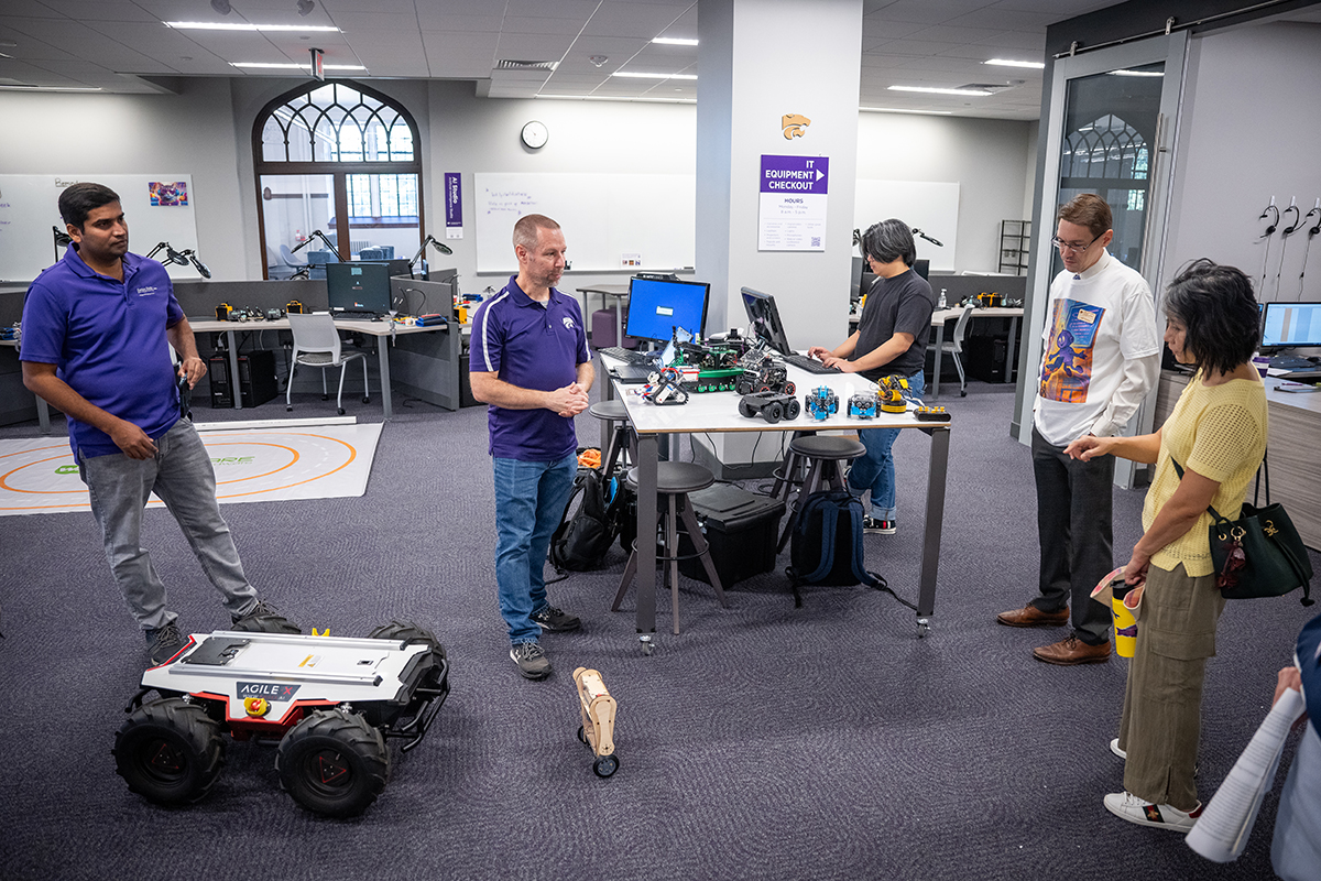 A group of people stand around several robotics on the ground
