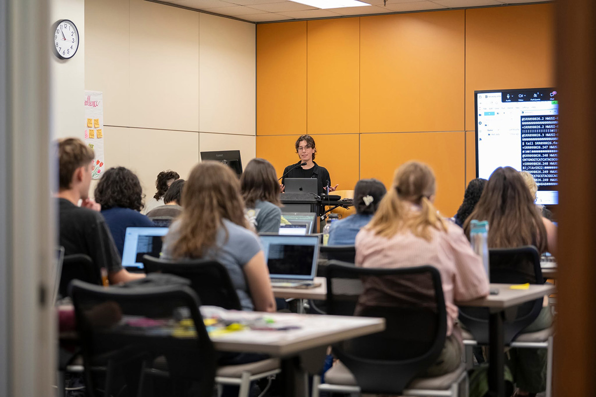 A female instructor teaches a lecture to a classroom of college students.