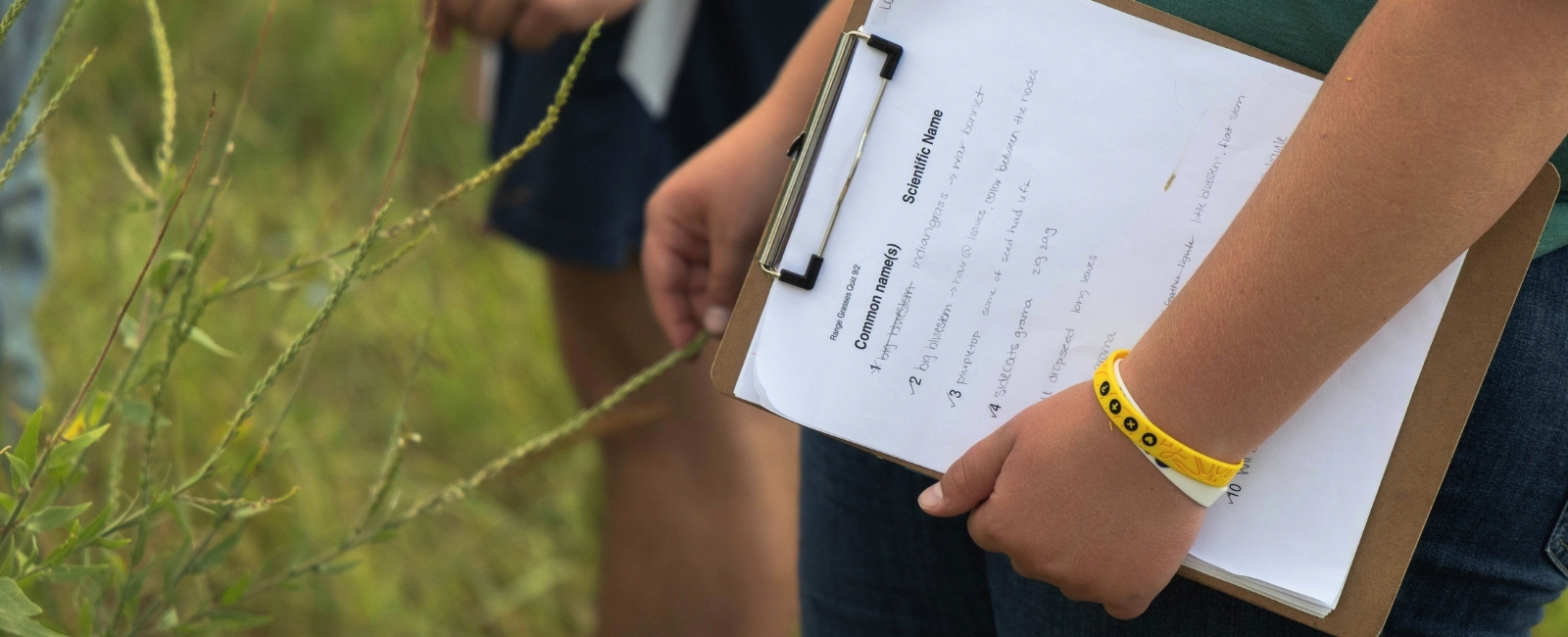 A close-up image of a student's hand holding a clipboard out in the grasslands at Rannell's Ranch.