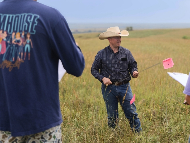 Colin Tobin stands in the tallgrass on the Rannells Ranch property during a class. He holds pink metal marking flags used to identify grass areas.