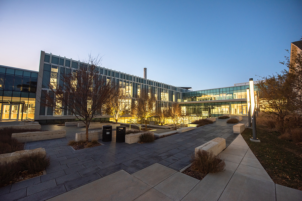 A night shot shows a limestone and glass college hall's exterior.