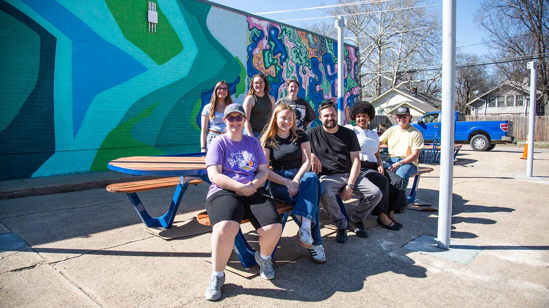 A group of students pose for a portrait on outdoor benches next to an art center building.