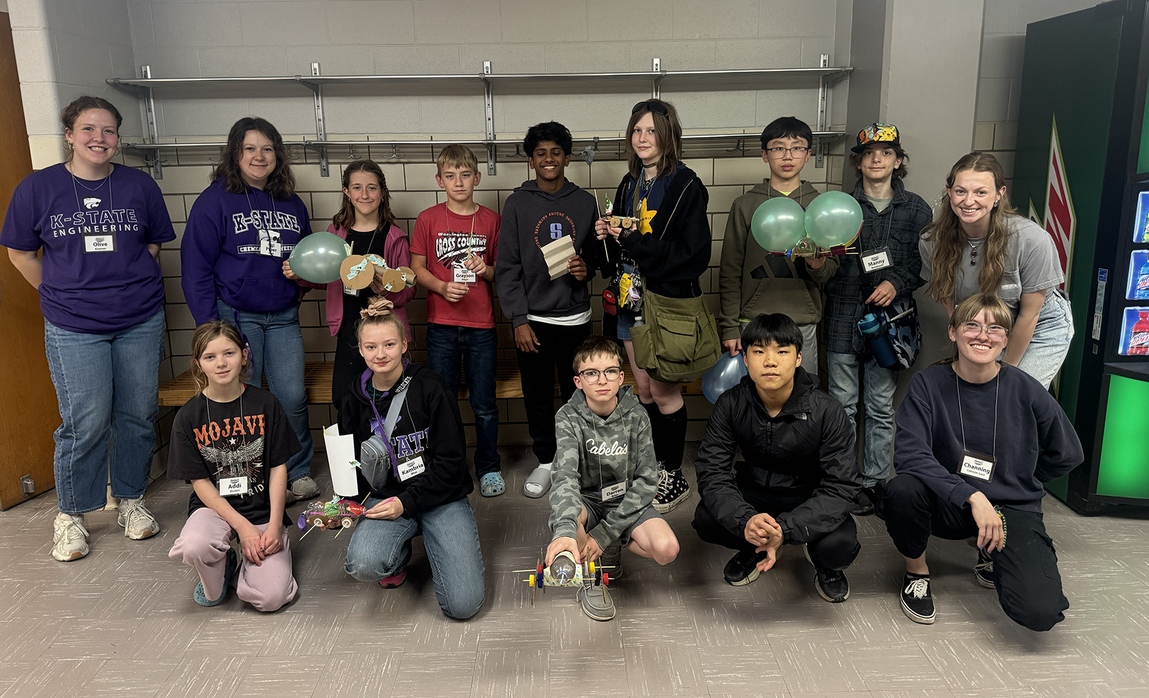 A group photo of middle school participants in a workshop. Some of the students hold cars they made and some have balloons.