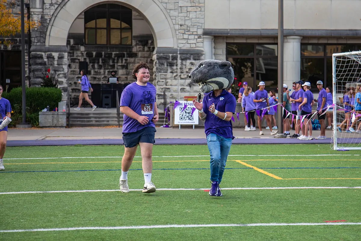 Willie the Wildcat running and cheering on a student to the finish line.