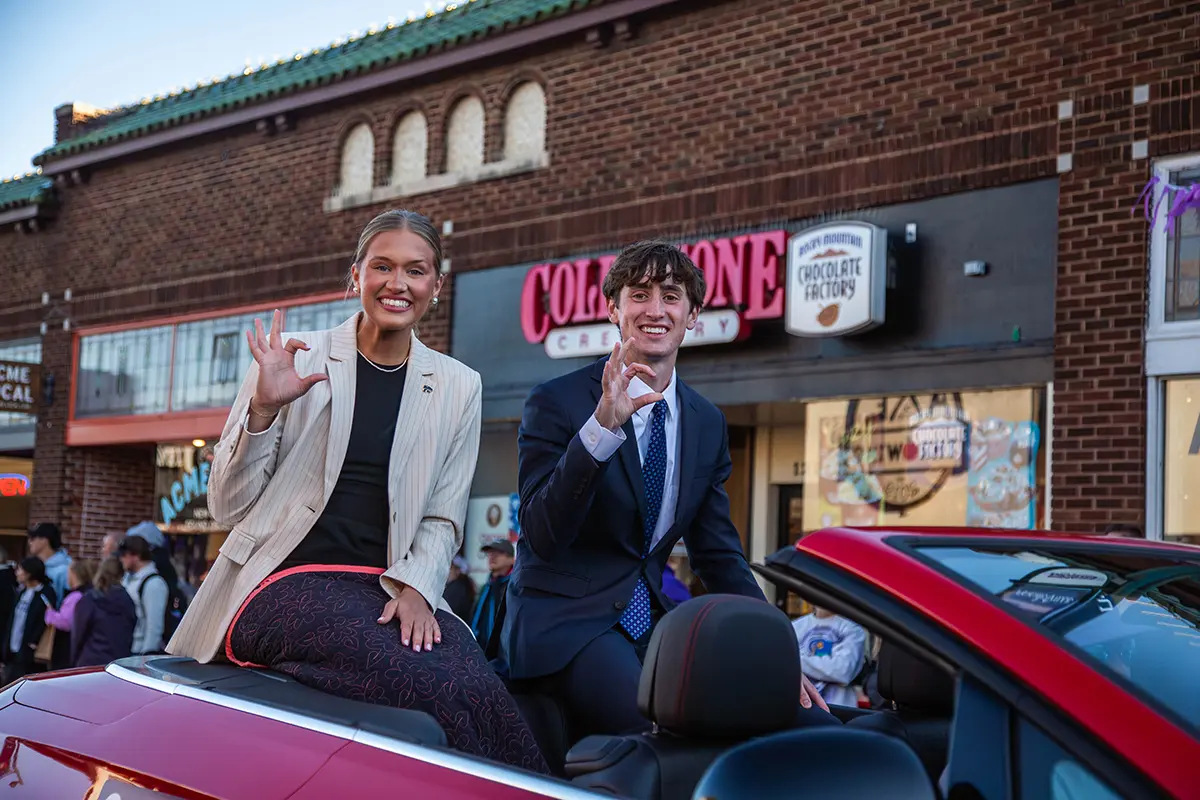 Two student ambassadors sitting in the back of a convertable car and waving at the crowd.