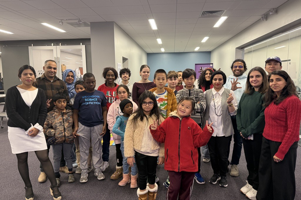 Several K-12 students pose with college graduate students in a classroom.