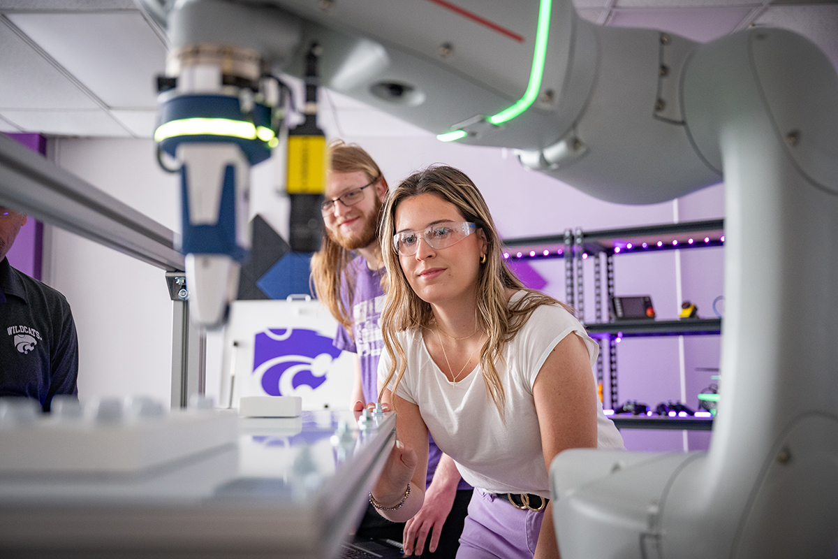 A pair of college students interact with a robotic arm in a lab.