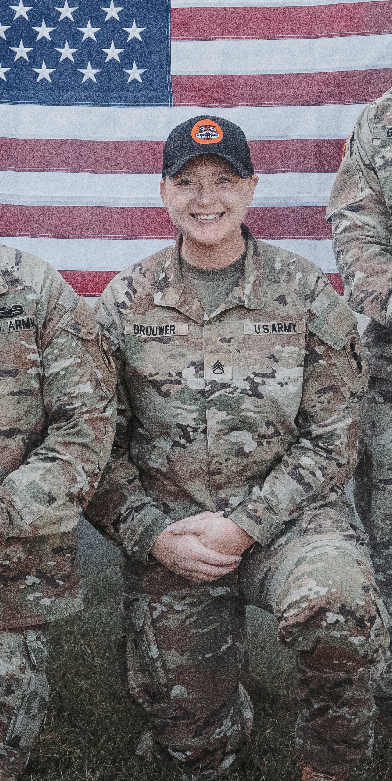 A woman in an Army uniform smiling for a photo in front of the U.S. flag.
